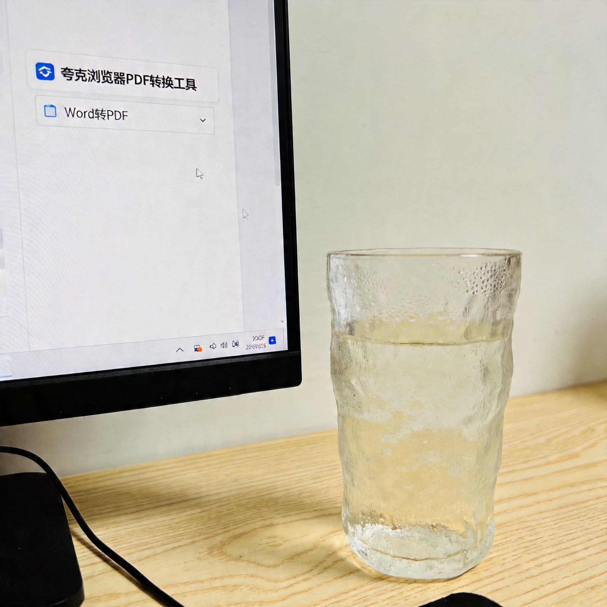 电脑桌的电脑屏幕显示夸克浏览器PDF转换工具界面，页面上有Word转PDF的选项，旁边放着半杯温水，室内自然光