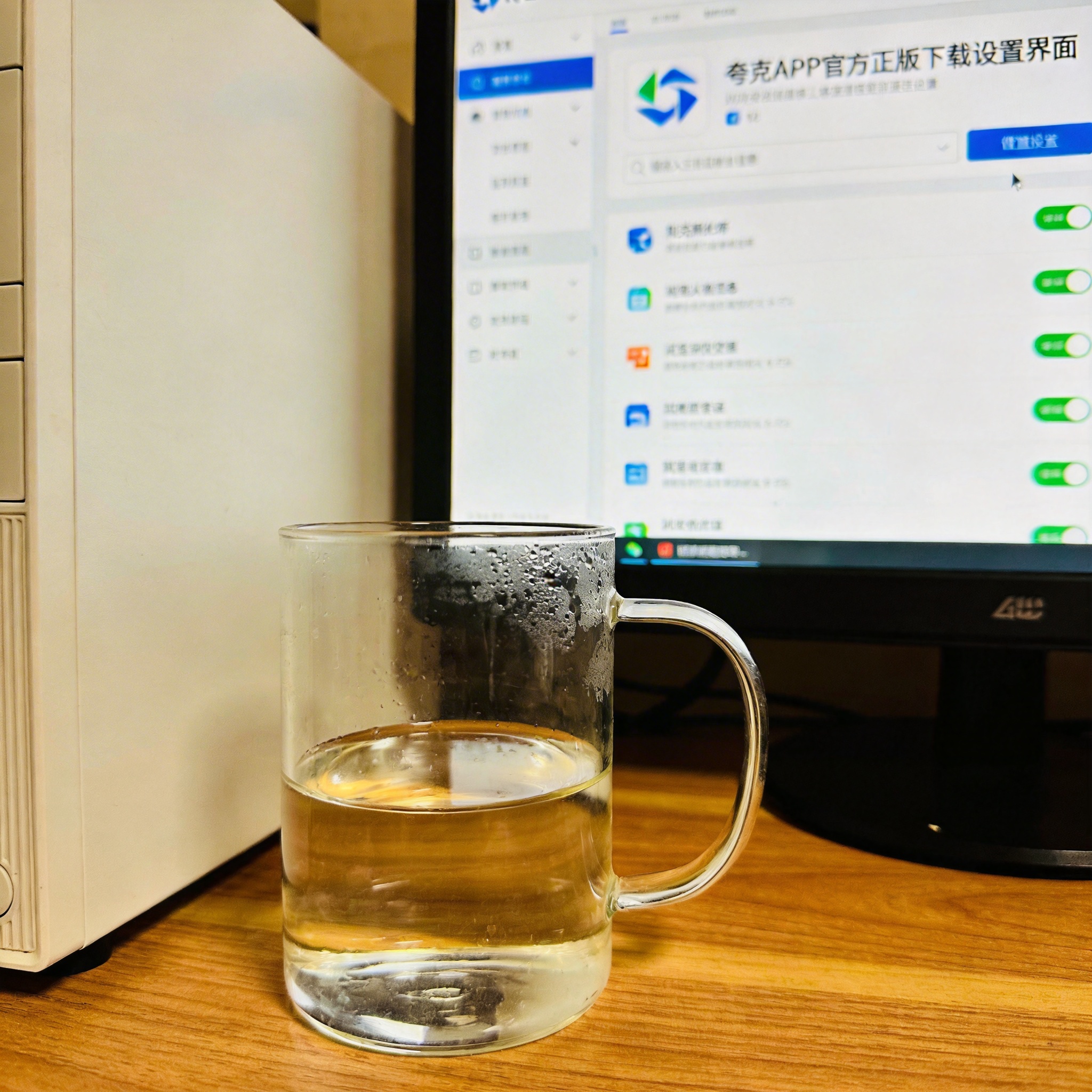 书桌上的主机，屏幕显示夸克 APP 官方正版下载设置界面，桌角放着水杯，自然光