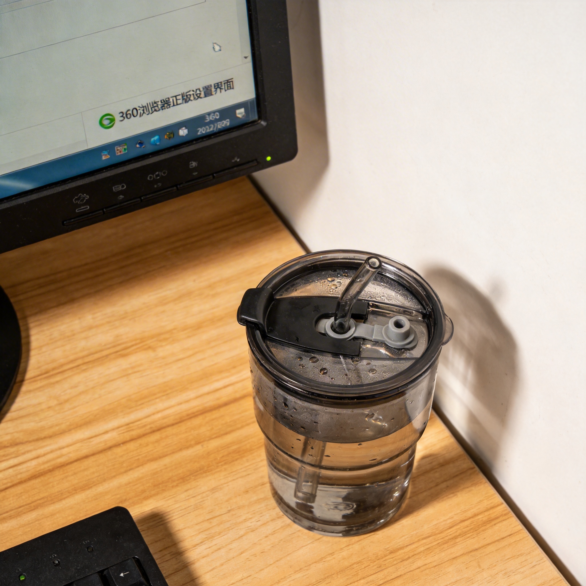 书桌上的主机，屏幕显示360 浏览器正版设置界面，桌角放着水杯，自然光