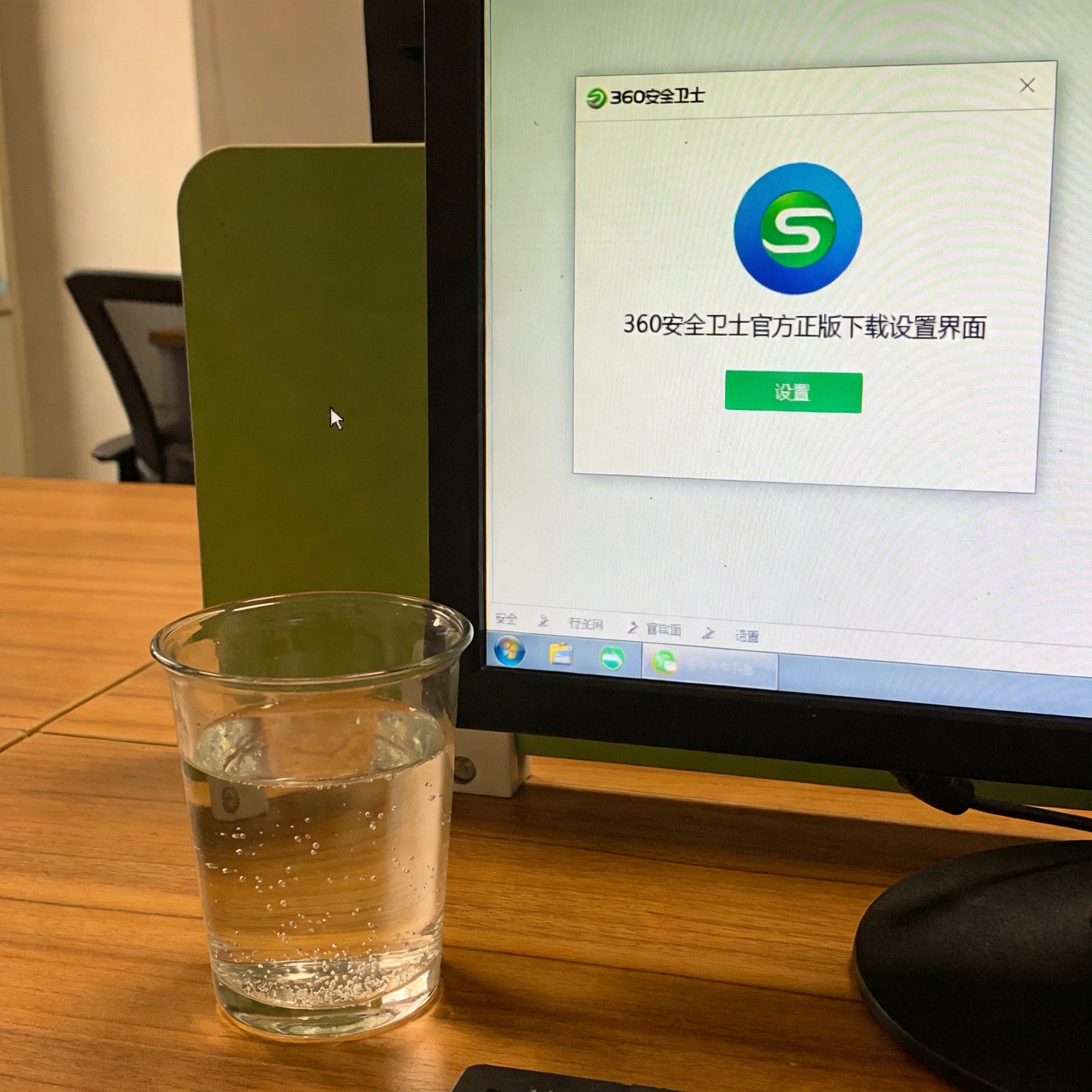 书桌上的电脑，屏幕显示360 安全卫士官方正版下载设置界面，桌角放着水杯，自然光