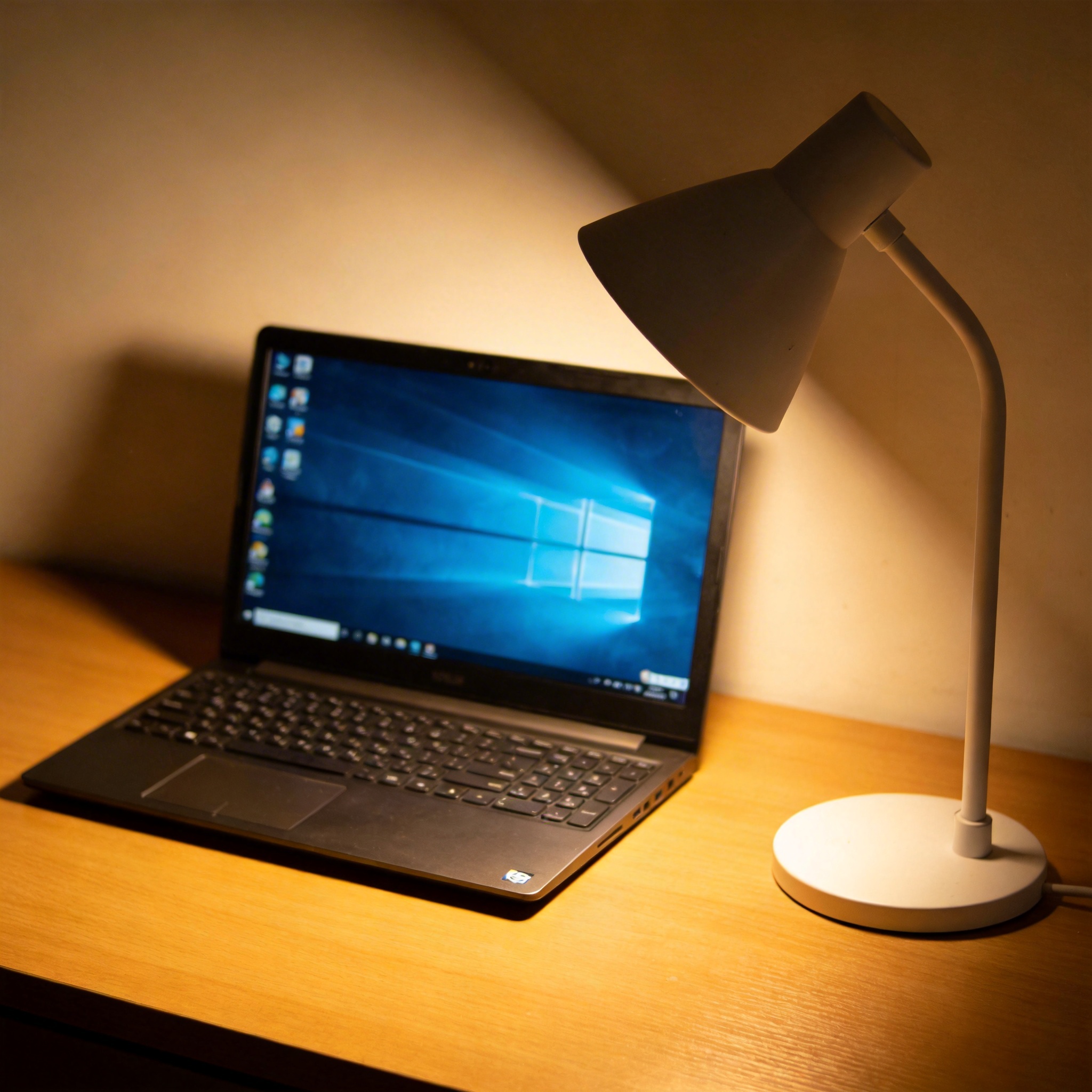 电脑桌上的电脑，屏幕显示Windows桌面，旁边放着台灯