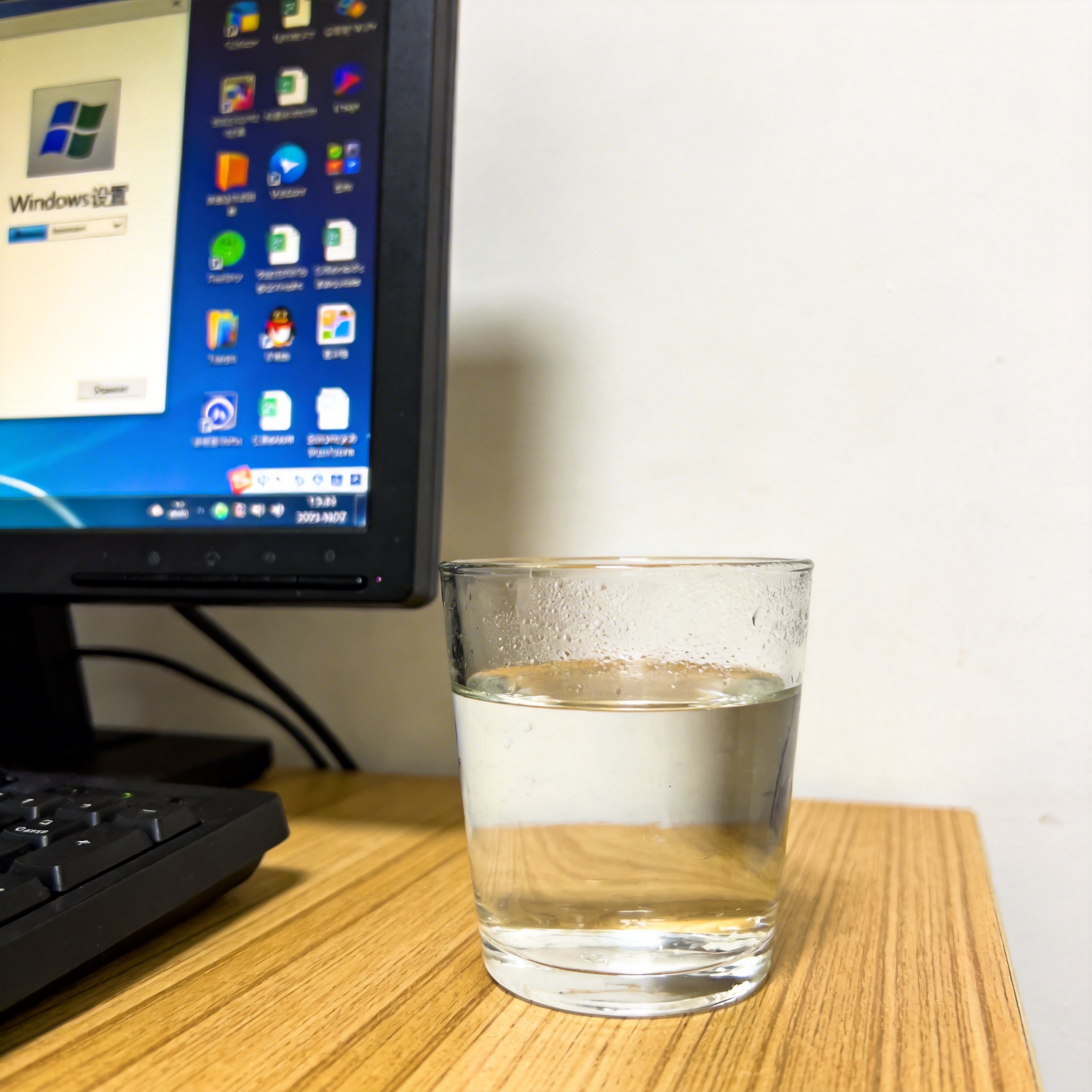 书桌上的主机，屏幕显示Windows设置界面，桌角放着水杯，自然光