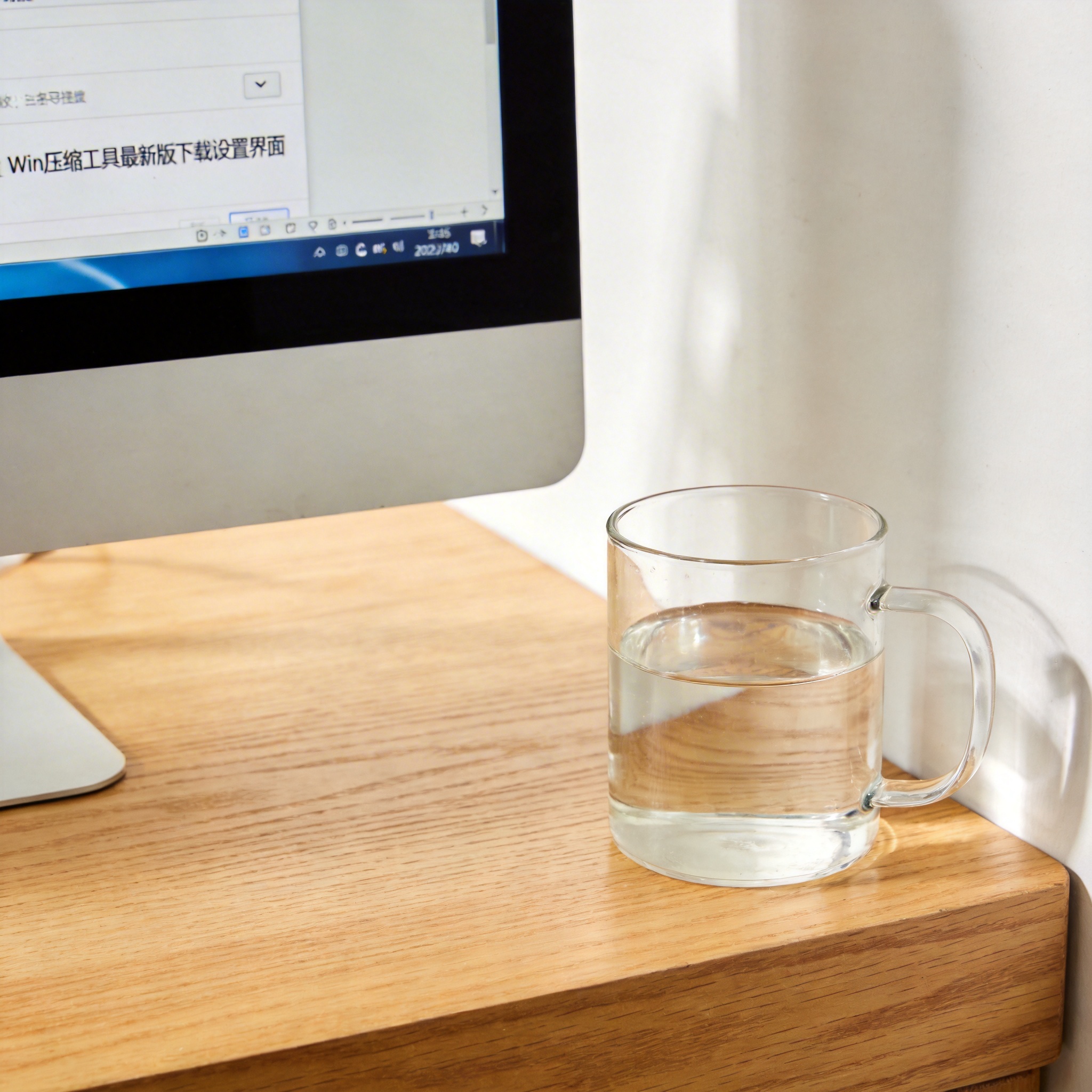 书桌上的主机，屏幕显示win 压缩工具最新版下载设置界面，桌角放着水杯，自然光