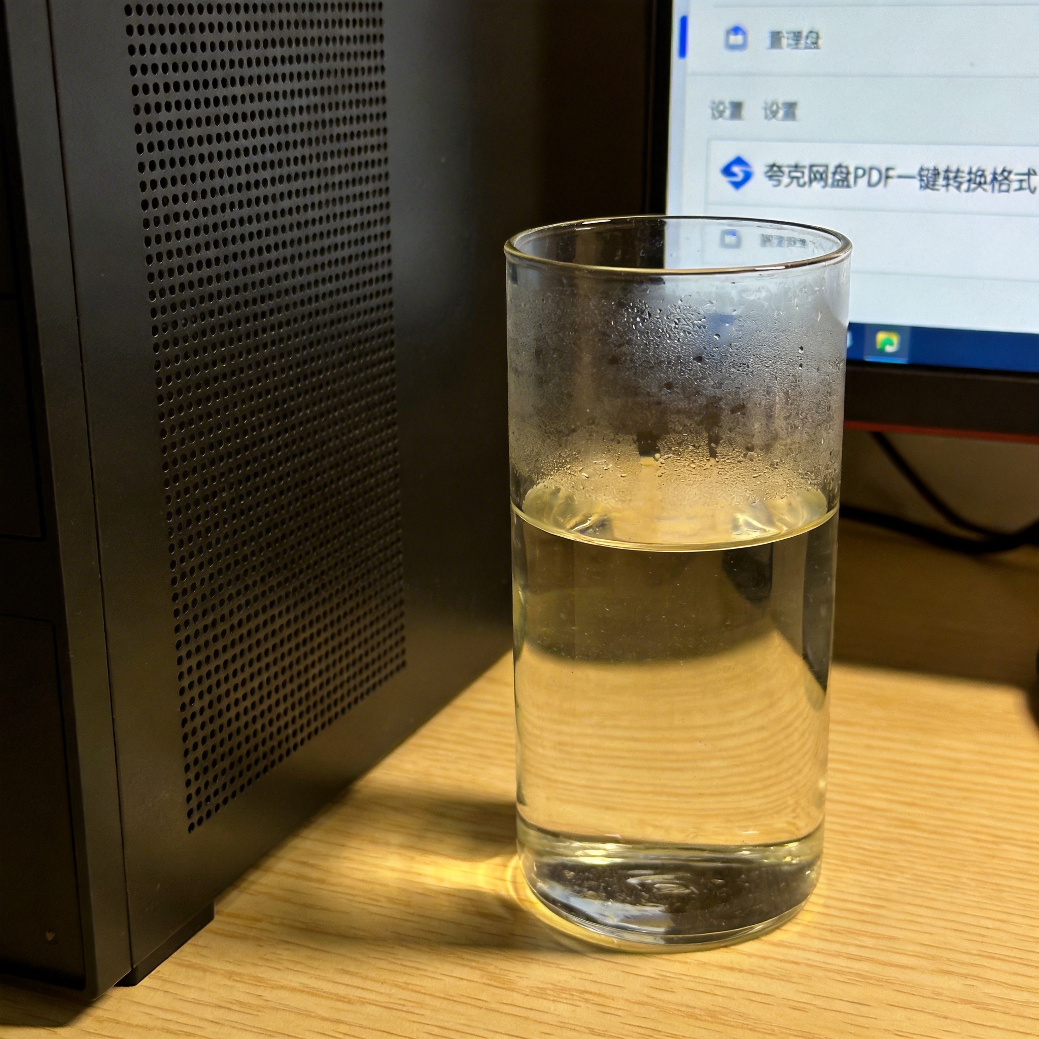 书桌上的主机，屏幕显示夸克网盘 PDF 一键转换格式设置界面，桌角放着水杯，自然光