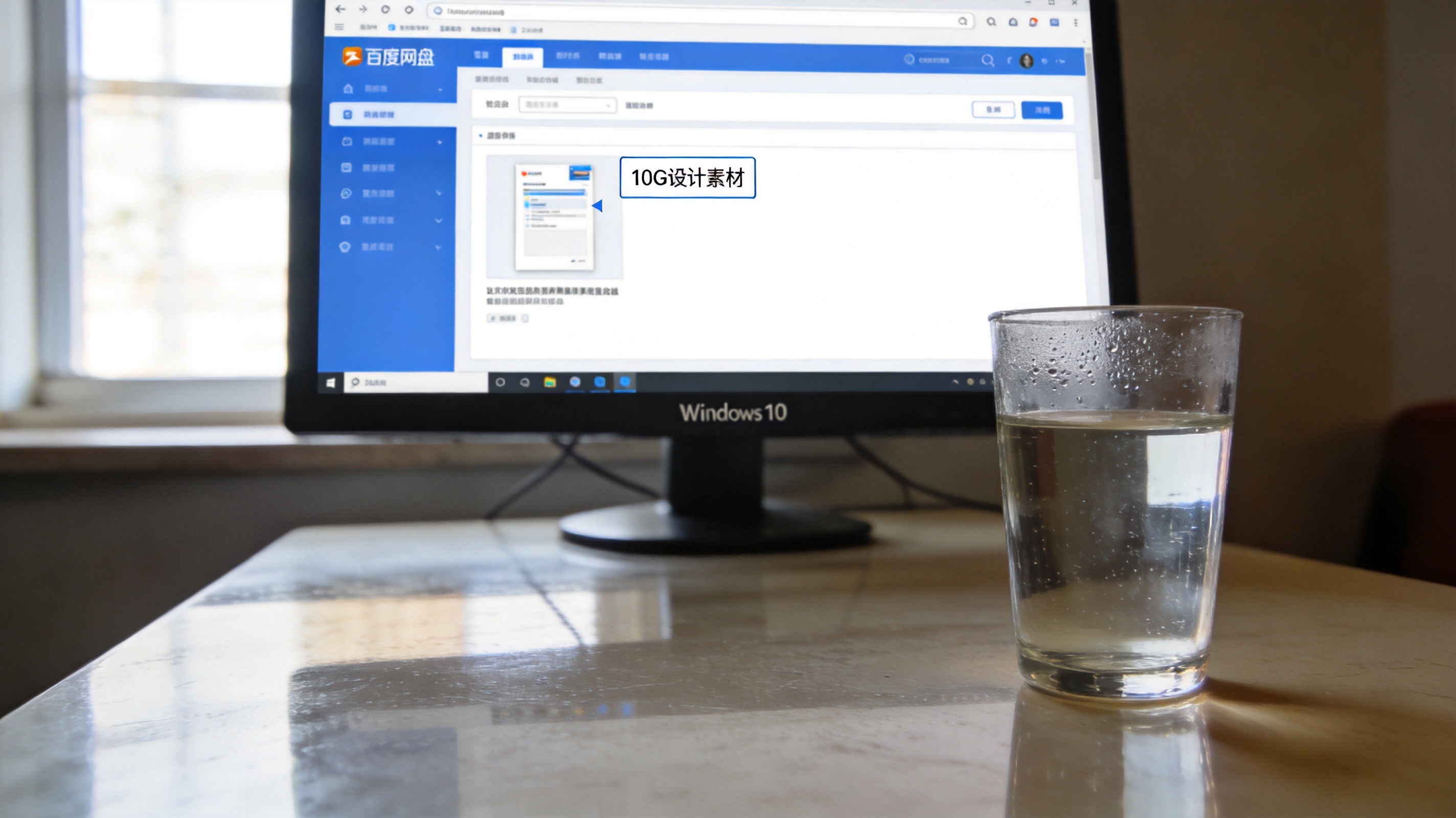 Windows10系统的电脑桌面，屏幕显示百度网盘网页版界面，页面里有10G大小的设计素材文件，桌面放着半杯温水，室内自然光