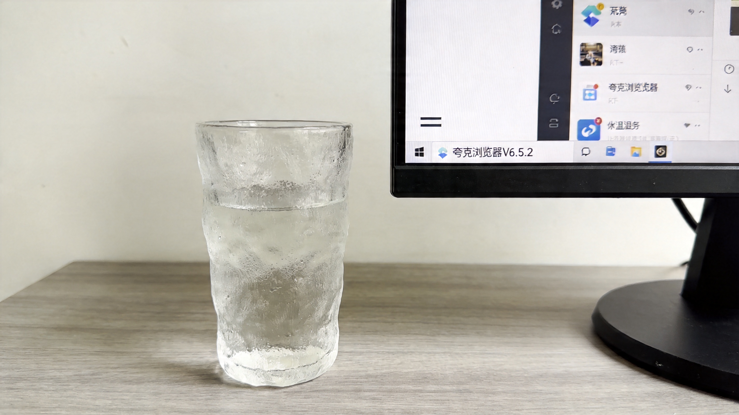 电脑桌面，屏幕显示夸克浏览器V6.5.2版本的底部三条杠菜单界面，旁边放着半杯温水，室内自然光