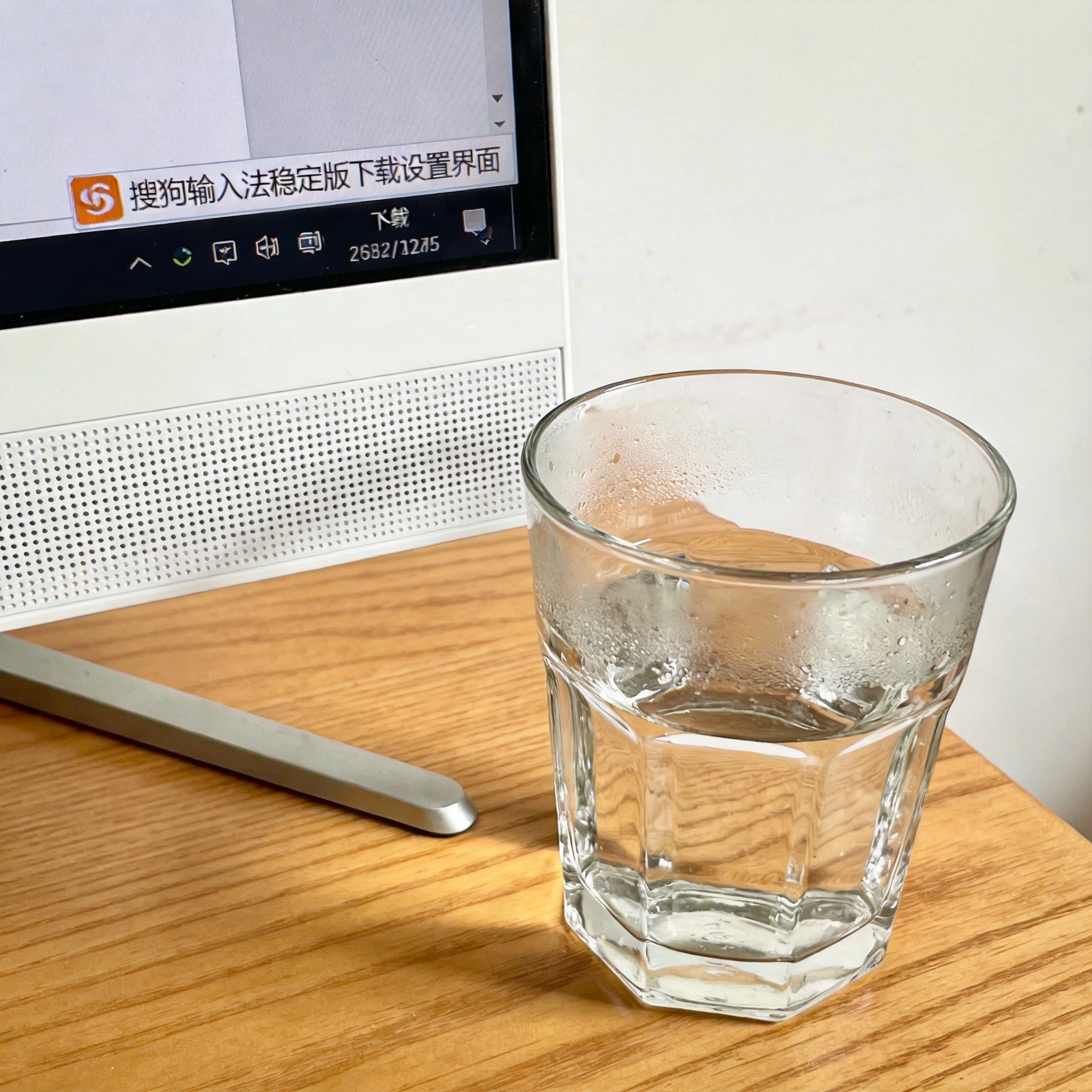 书桌上的主机，屏幕显示搜狗输入法稳定版下载设置界面，桌角放着水杯，自然光
