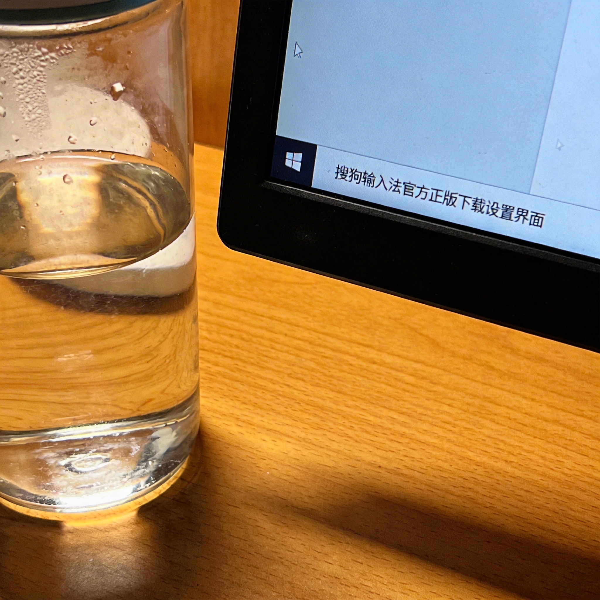 书桌上的屏幕，屏幕显示搜狗输入法官方正版下载设置界面，桌角放着水杯，自然光