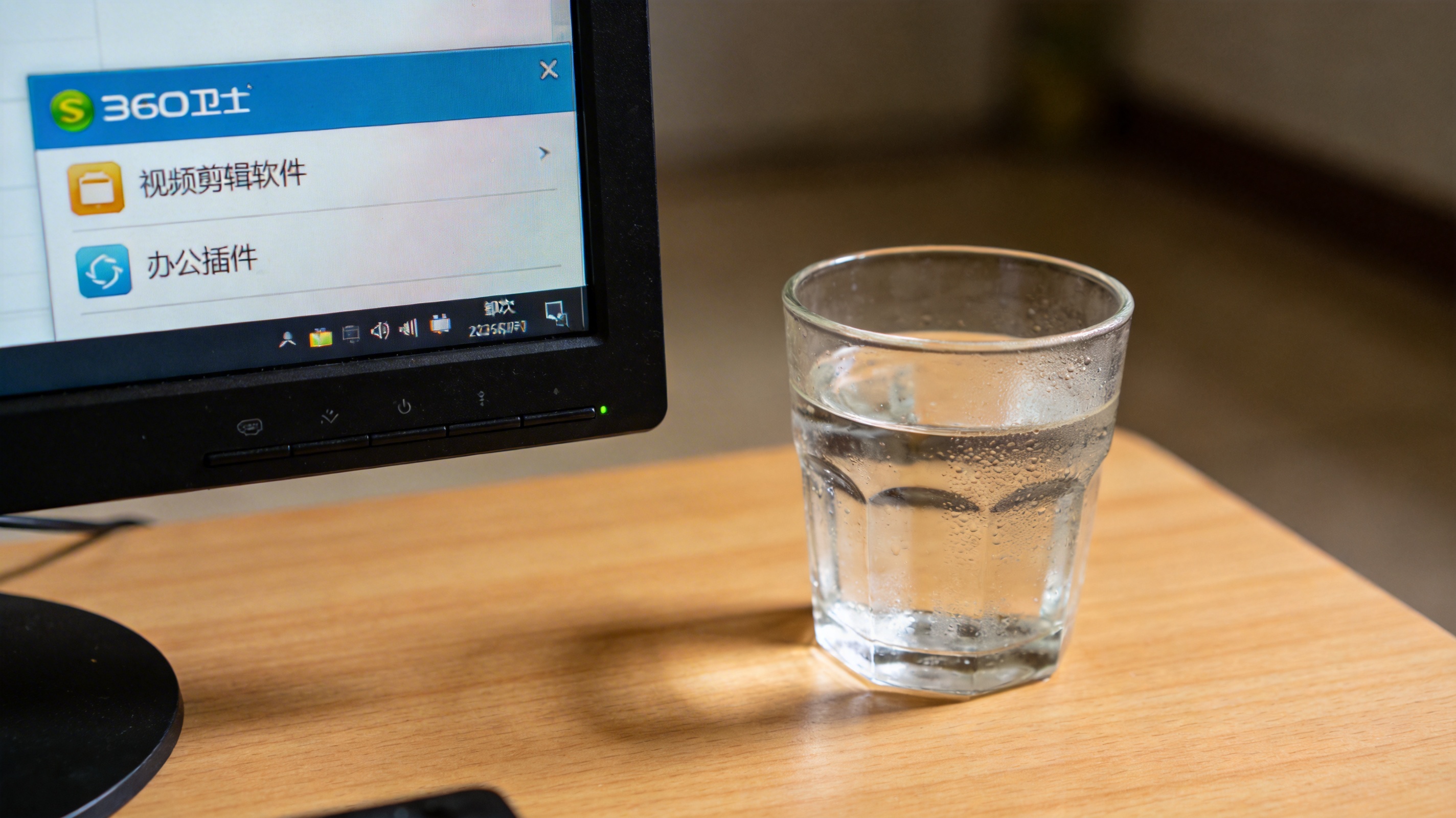 电脑桌面，屏幕显示360卫士软件卸载界面，界面列出视频剪辑软件和办公插件，旁边放着半杯凉白开，室内自然光
