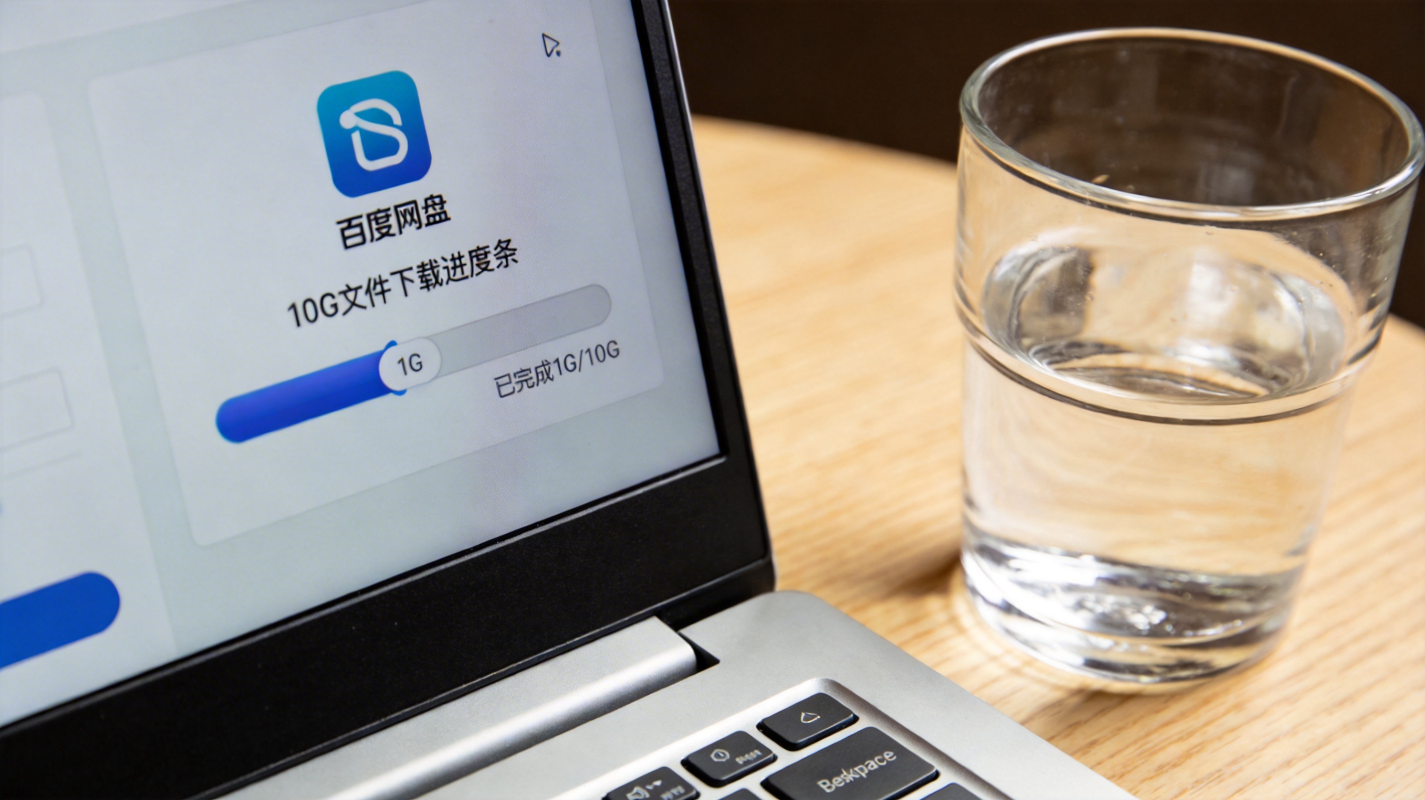 电脑桌面，屏幕显示百度网盘手机端模拟界面，10G文件下载进度条显示完成1G，旁边放着水杯，室内自然光