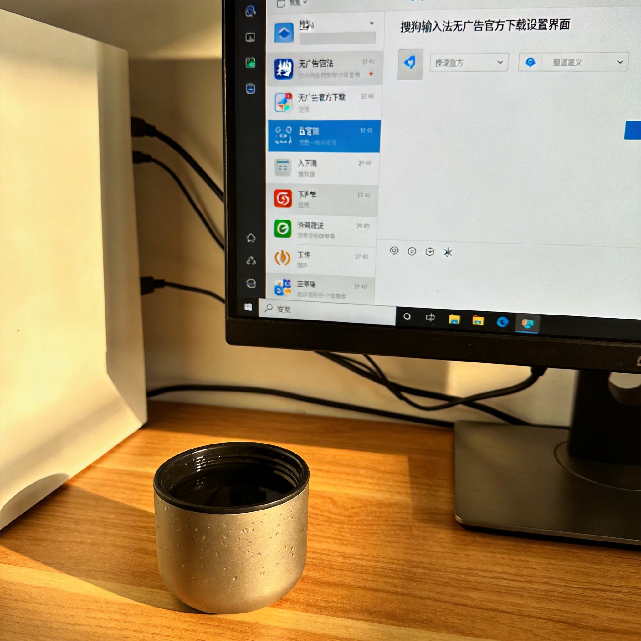 书桌上的主机，屏幕显示搜狗输入法无广告官方下载设置界面，桌角放着水杯，自然光
