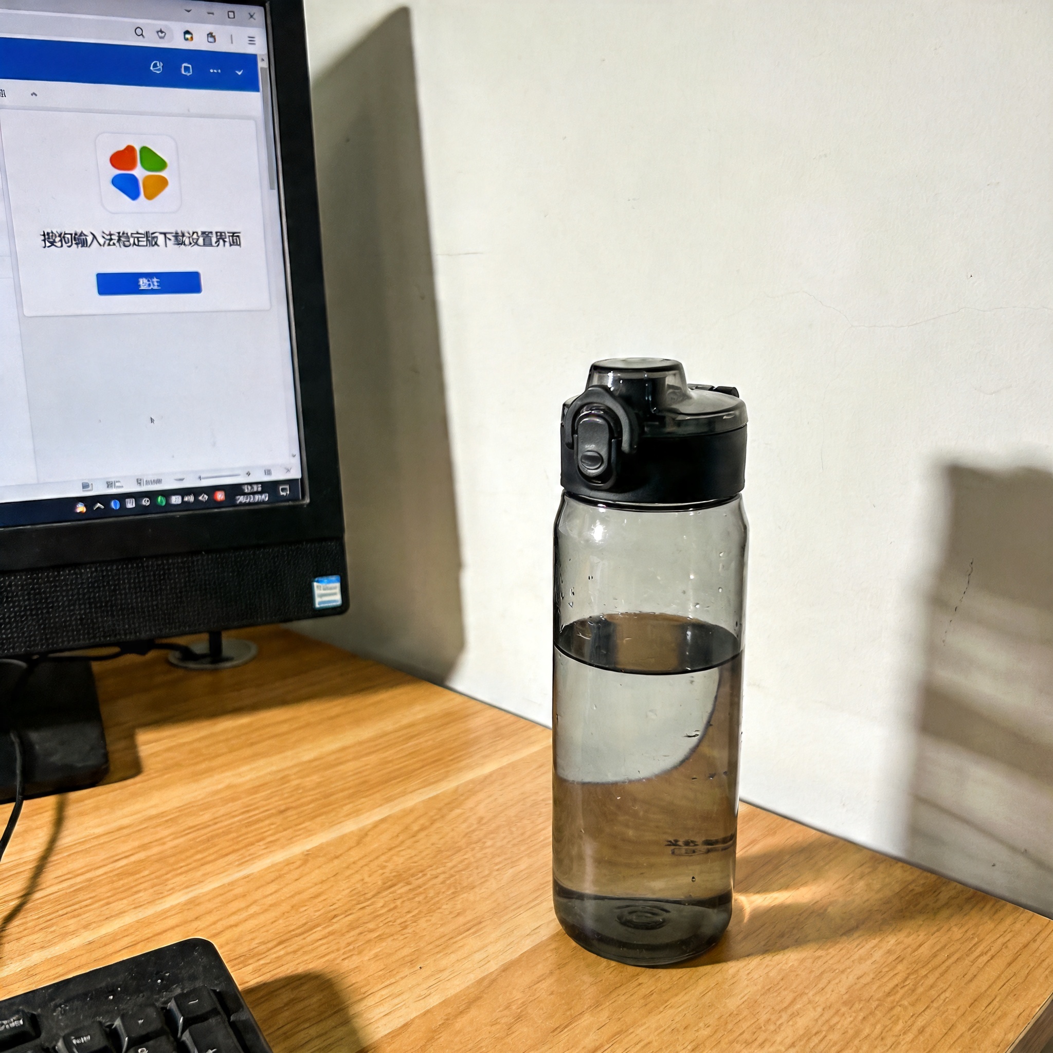 书桌上的主机，屏幕显示搜狗输入法稳定版下载设置界面，桌角放着水杯，自然光