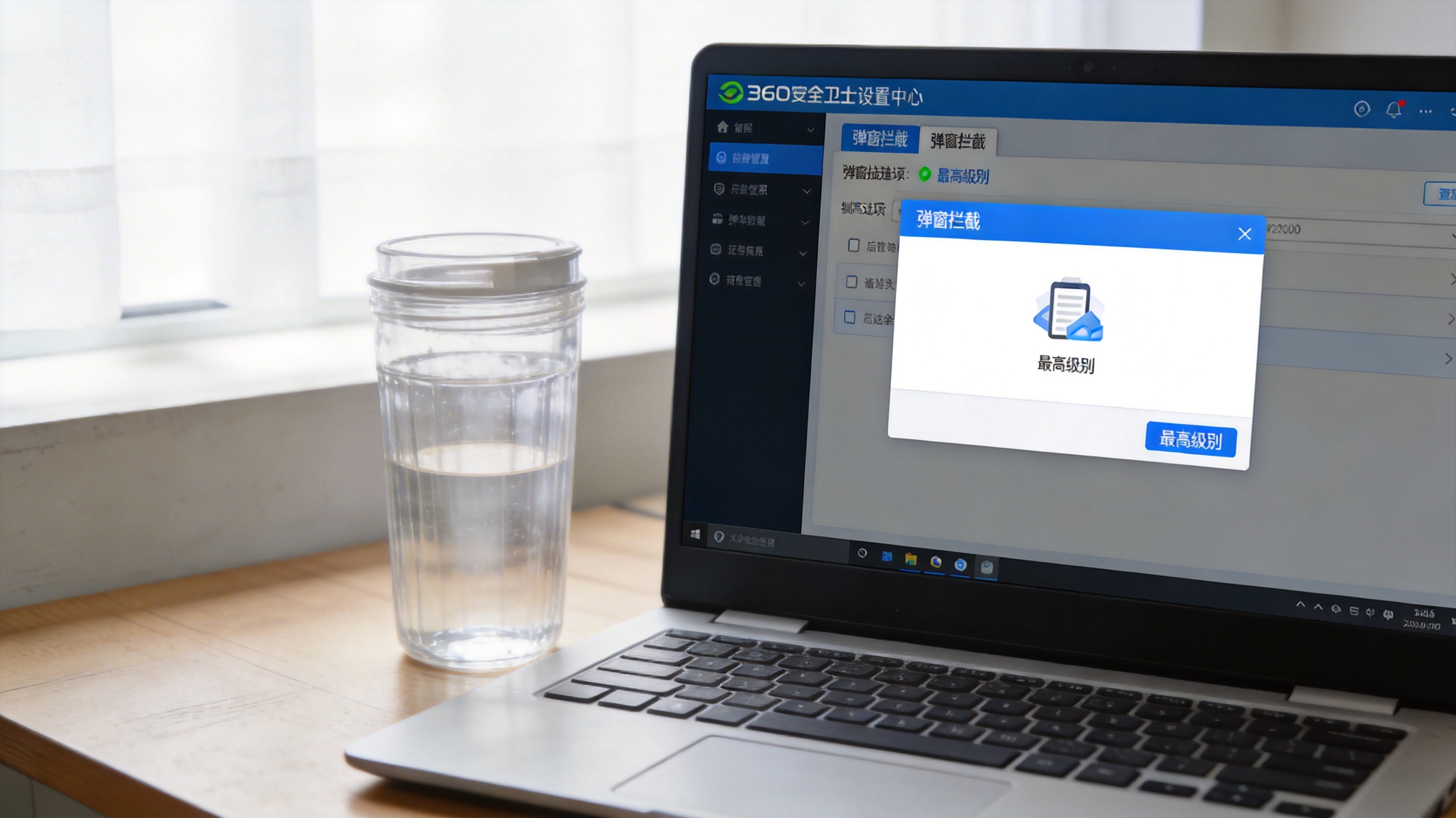 电脑桌面，屏幕显示360安全卫士设置中心界面，弹窗拦截选项调至最高级别，旁边放着半透明水杯，室内自然光