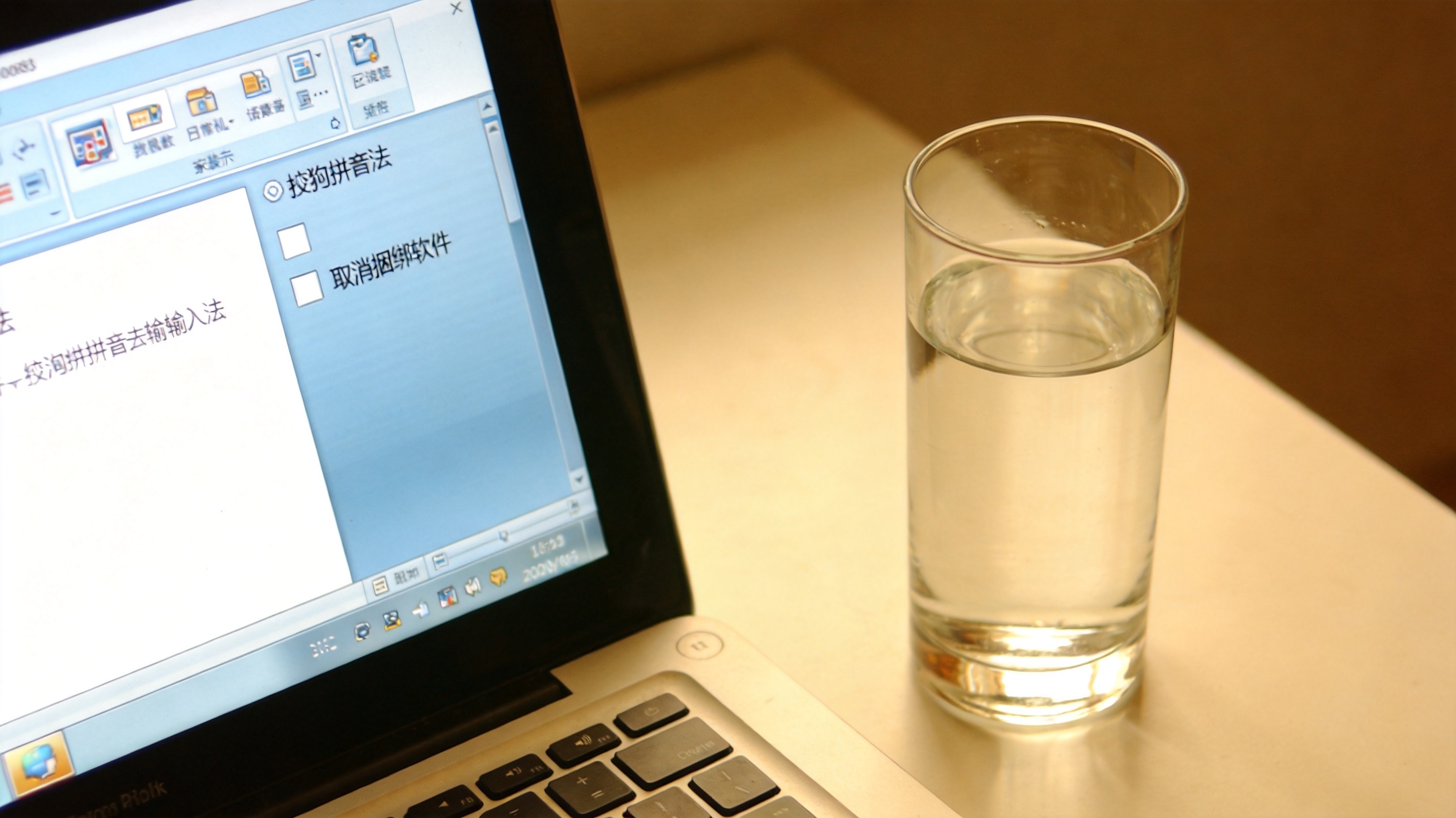 电脑桌面显示搜狗拼音输入法安装界面，界面上有取消捆绑软件的勾选框，旁边放着半杯温水，室内自然光