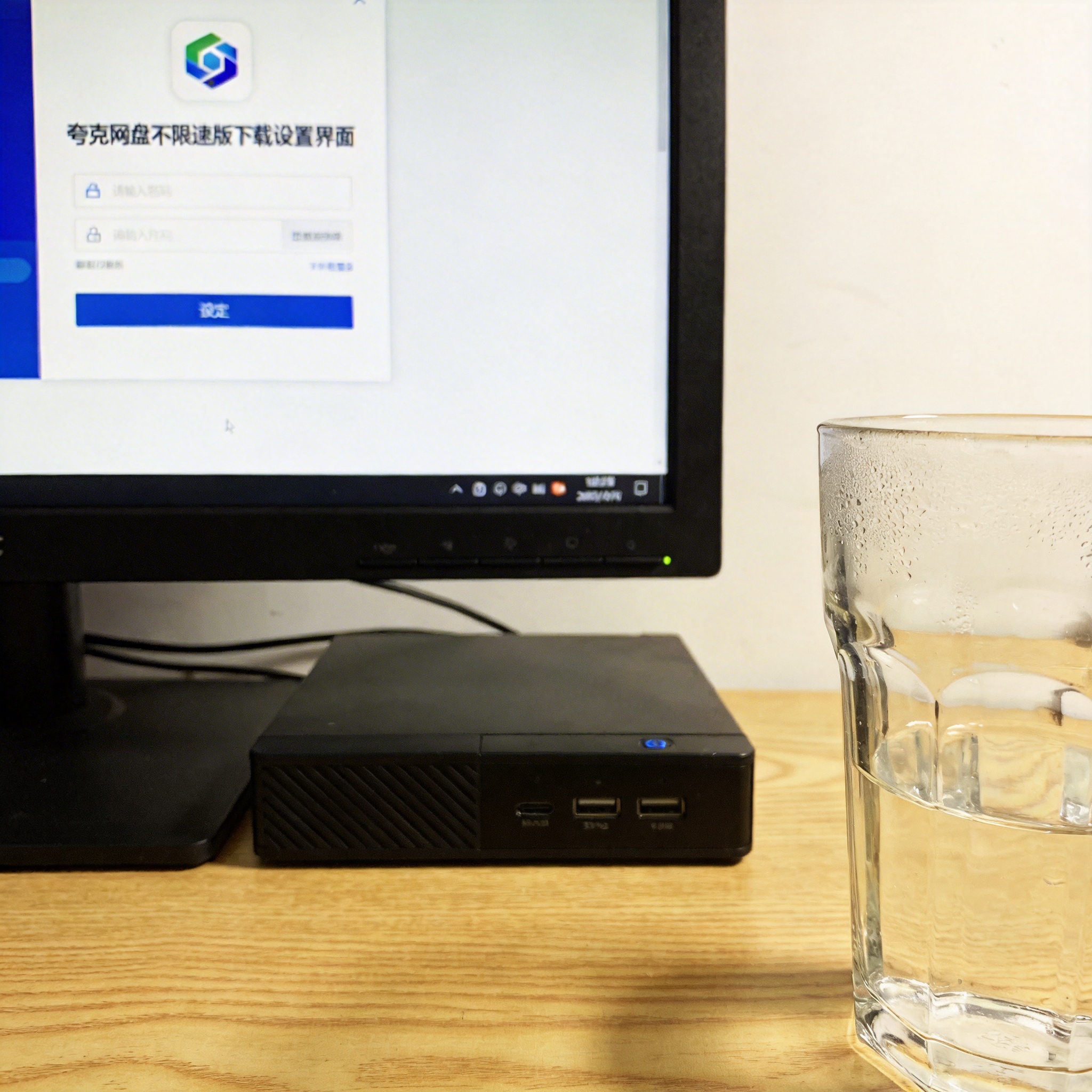 书桌上的主机，屏幕显示夸克网盘不限速版下载设置界面，桌角放着水杯，自然光