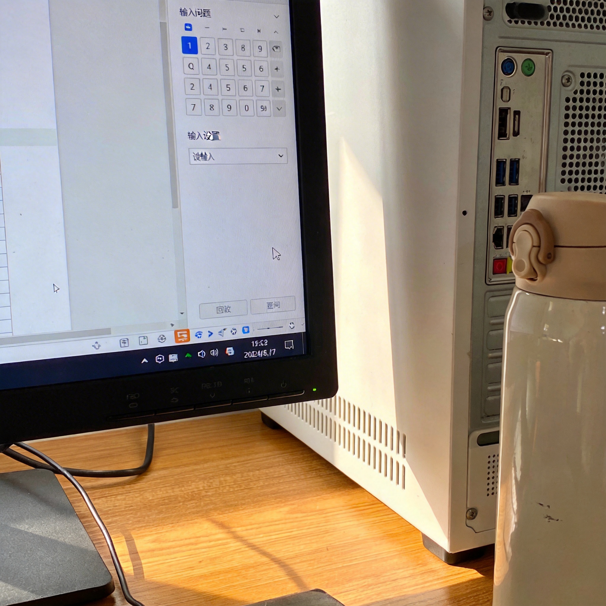 书桌上的主机，屏幕显示输入法设置界面，桌角放着水杯，自然光