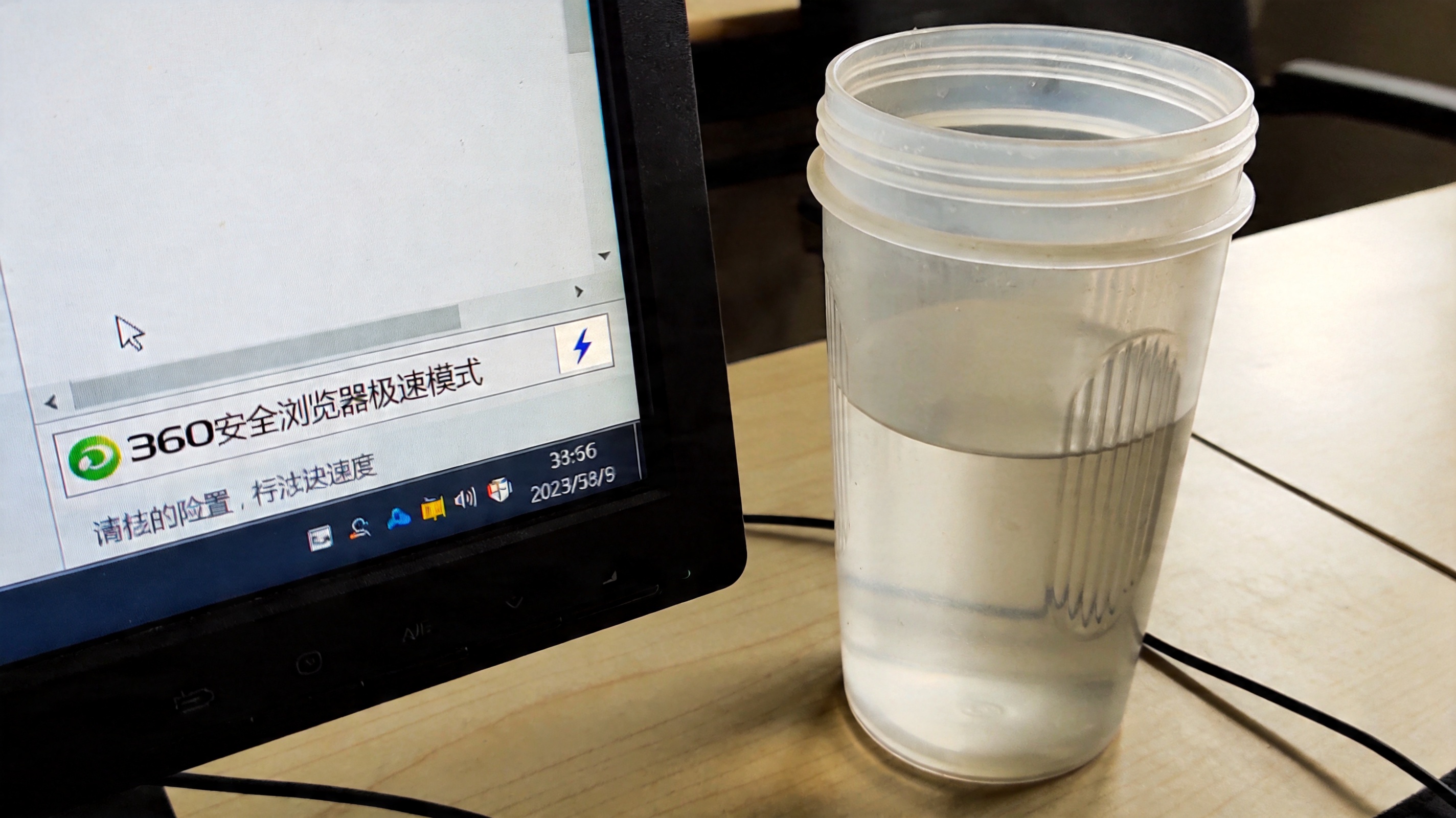 电脑桌面，屏幕显示360安全浏览器极速模式界面，地址栏右侧显示闪电图标，旁边放着半透明塑料水杯，室内自然光