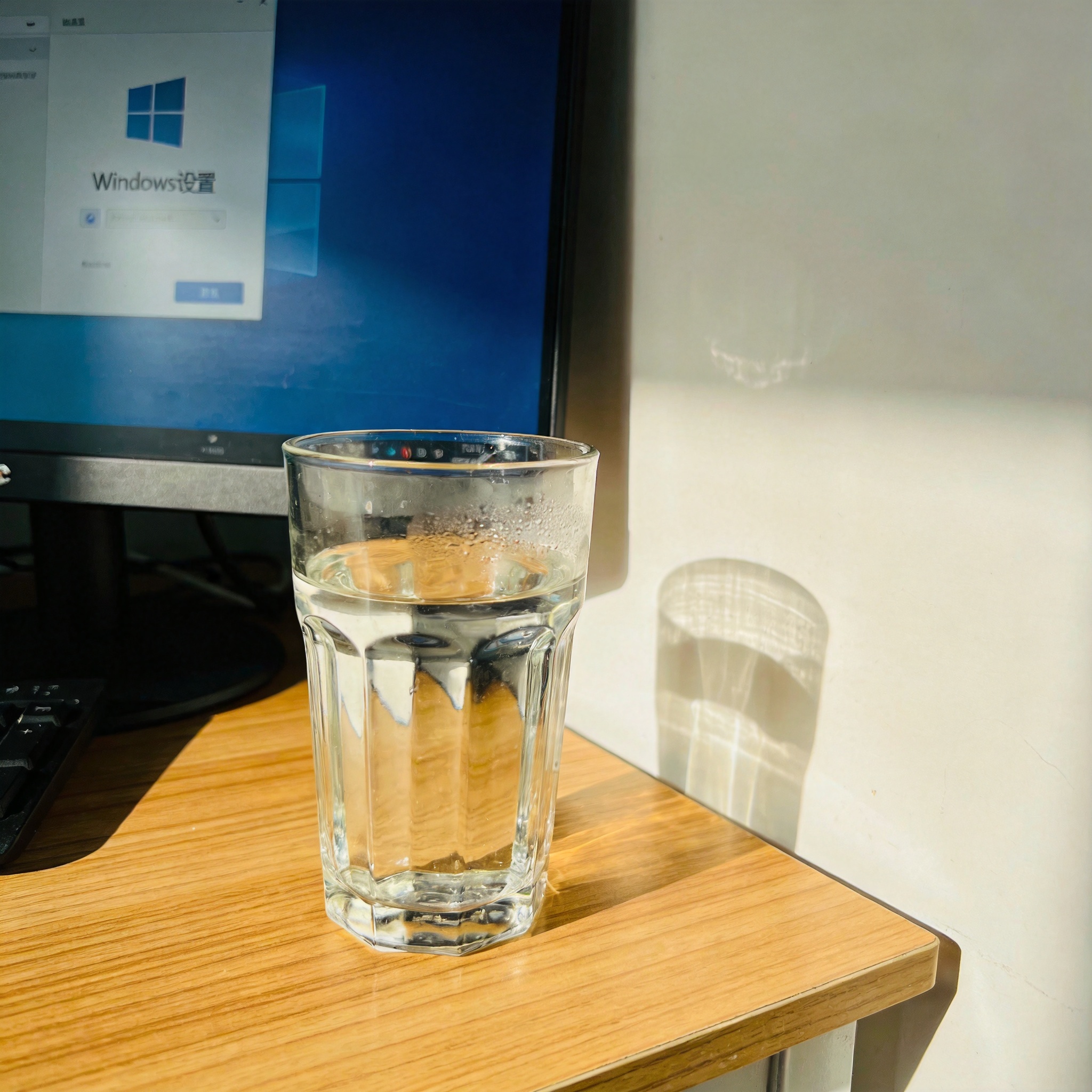 书桌上的电脑，屏幕显示Windows设置界面，桌角放着水杯，自然光