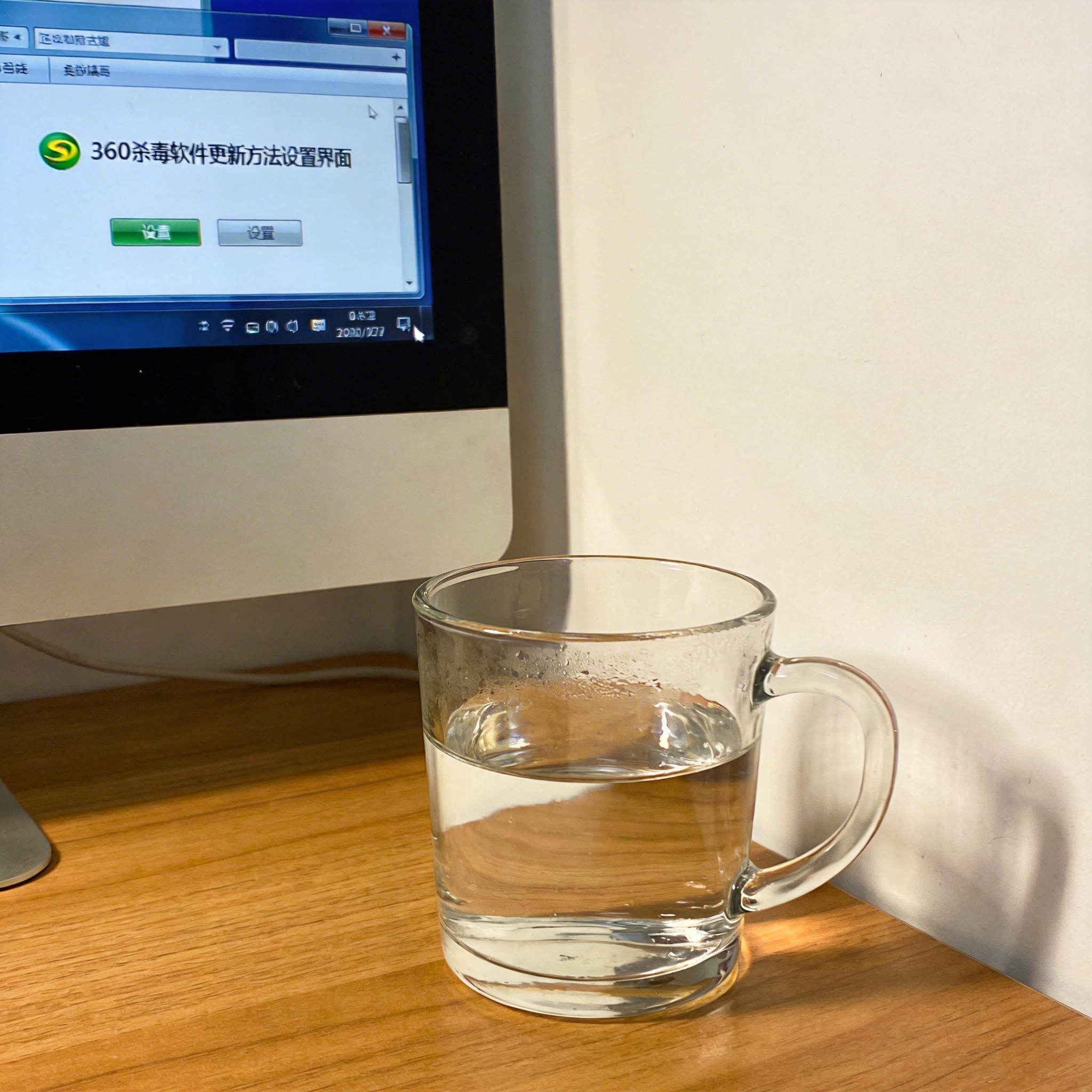 书桌上的主机，屏幕显示360 杀毒软件更新方法设置界面，桌角放着水杯，自然光