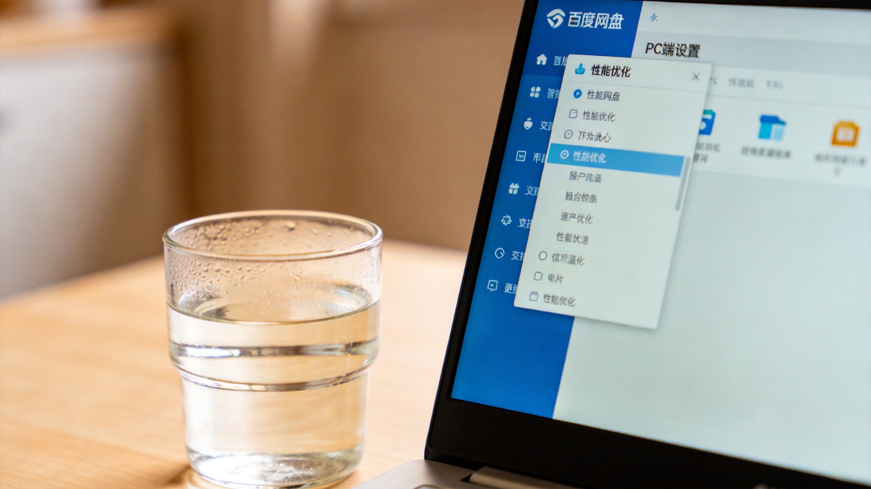 电脑桌面，屏幕显示百度网盘PC端设置界面，下拉菜单展开着“性能优化”选项，旁边放着半杯温水，室内自然光