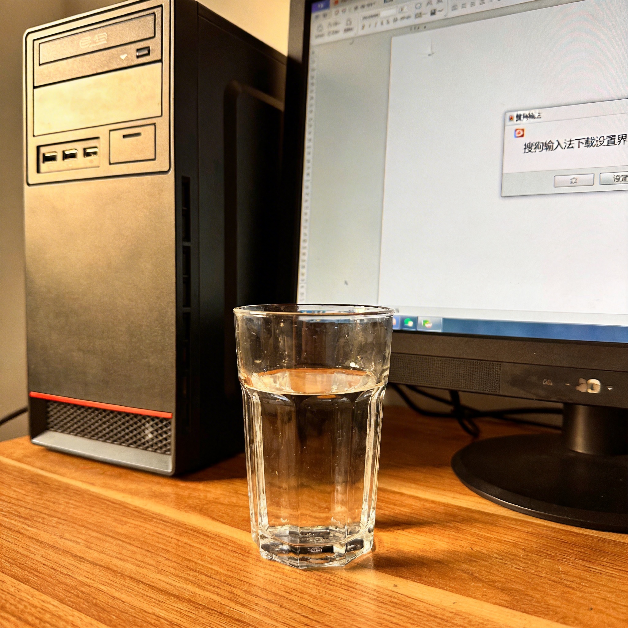 书桌上的主机，屏幕显示搜狗输入法下载设置界面，桌角放着水杯，自然光