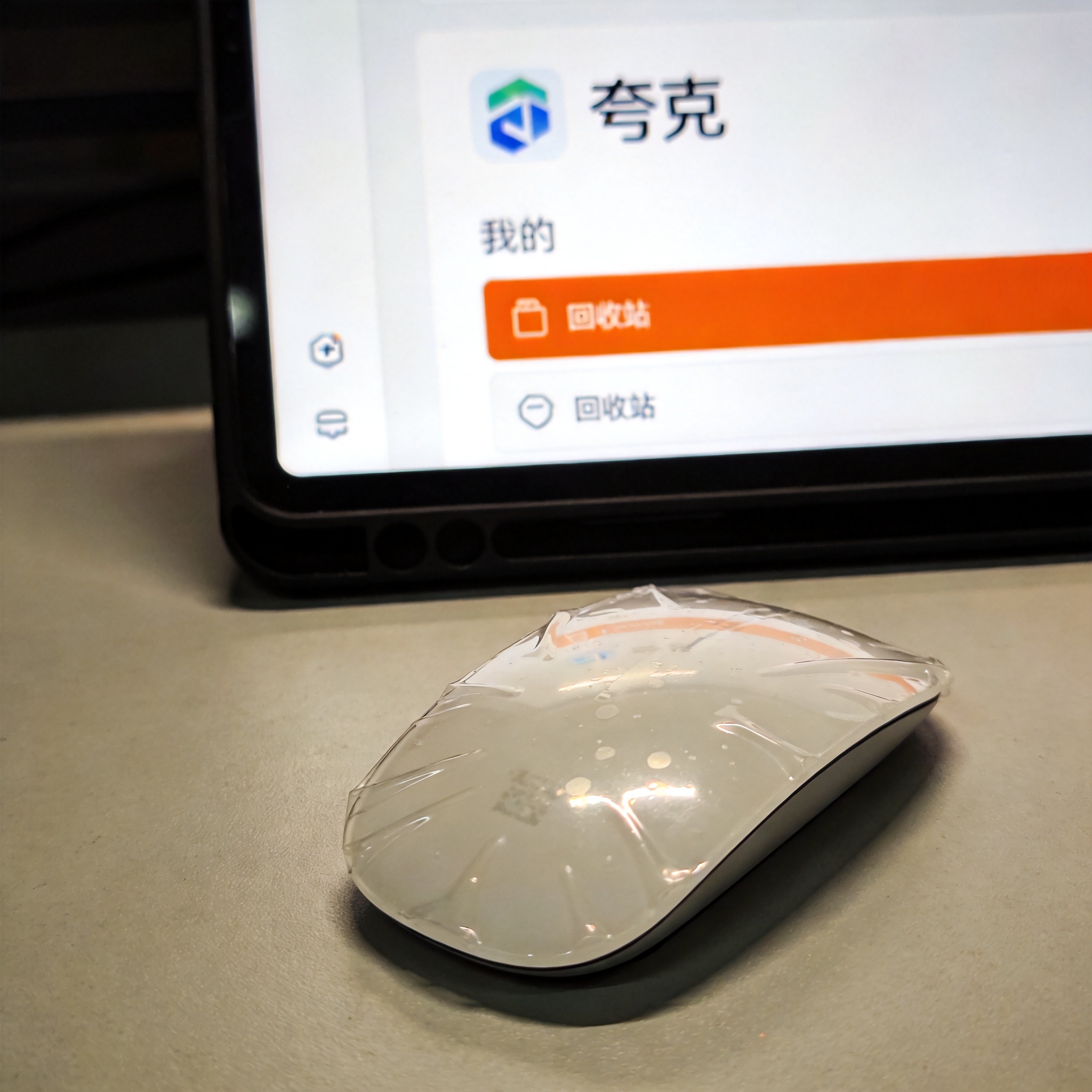 桌面的电脑屏幕显示夸克网盘“我的”页面，回收站入口高亮显示，屏幕光映在桌面的塑料鼠标上